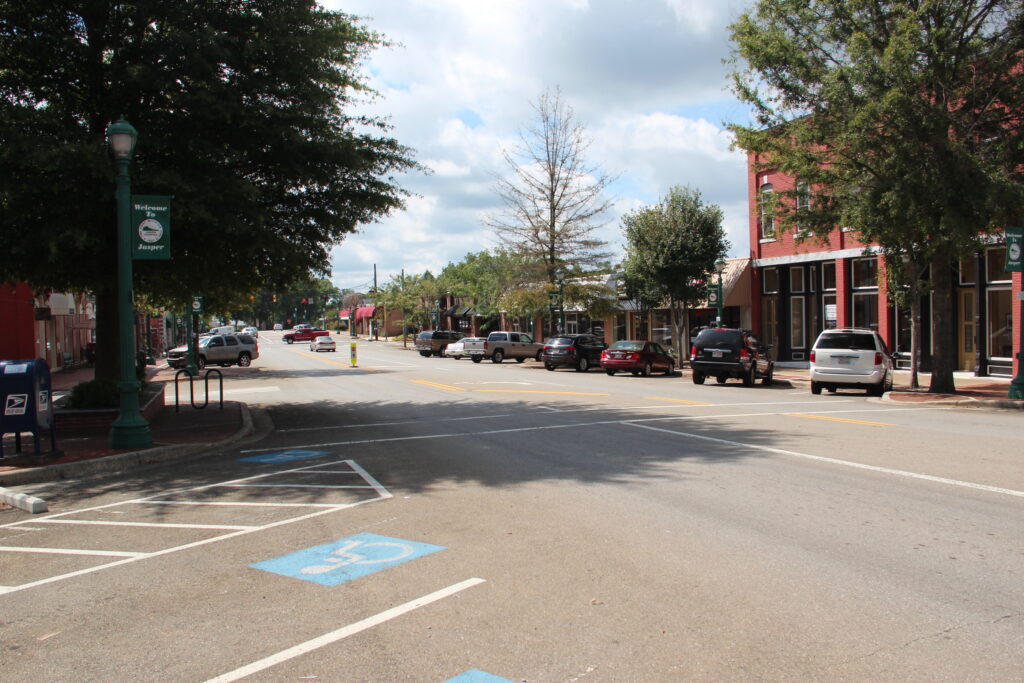Downtown Jasper, Georgia, featuring historic brick buildings, parked cars, and a welcoming “Welcome to Jasper” banner on a tree-lined street.